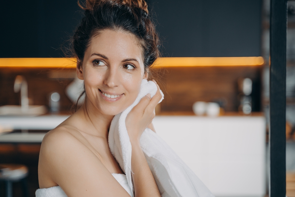 Smiling hispanic woman wiping face with white cotton towel after getting a hyrdrafacial in wayzata