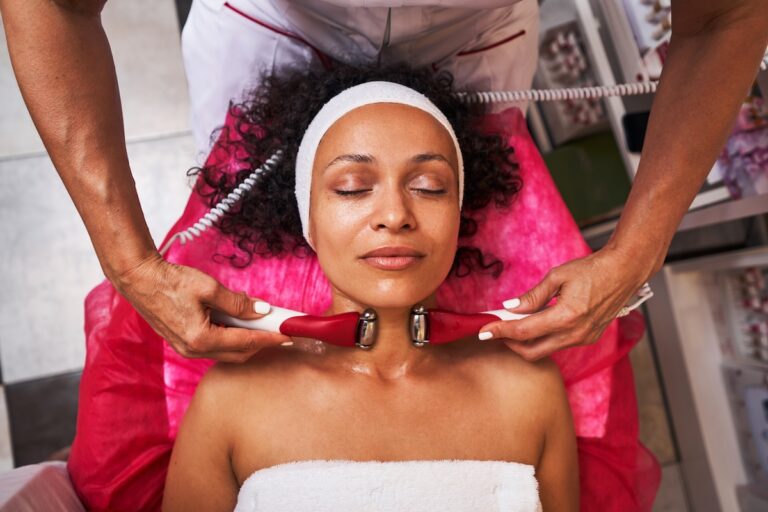 A woman with curly hair and a white headband receives a lymphatic drainage facial in Minneapolis